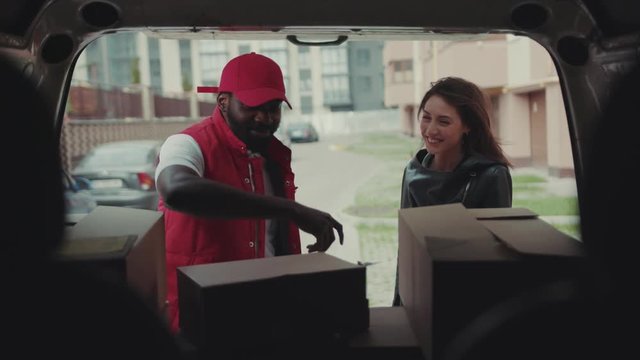 Courier African American gives a parce to a smiling woman after signing on delivery device cardboard technology box order post postal service device sunny beard covered load logistic mailman