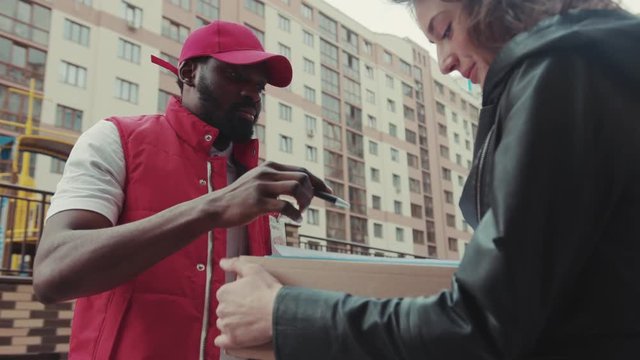 Face courier African American gives a parce to a woman after signing on delivery device cardboard technology box order post postal service device sunny beard covered load logistic slow motion