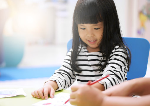Asian children cute or kid girl smile and learning for coloring or paint on white paper with teacher or mother at nursery or school and kindergarten on soft focus and sunlight on window