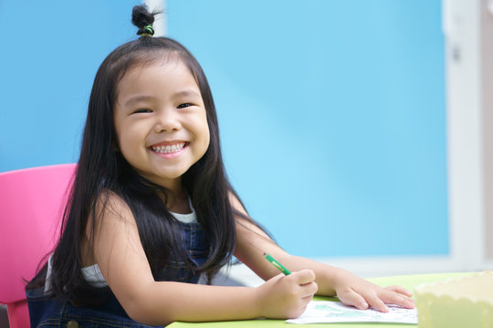 Asian children cute or kid girl happy smile and learning for coloring or paint on white paper with teacher or mother at kindergarten and nursery or school on colorful and blue background