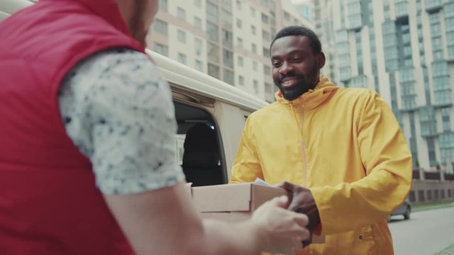 courier African American gives a parce to a man after signing on delivery device cardboard technology box order post postal service device sunny beard covered load logistic mailman