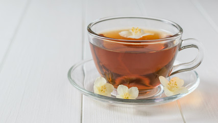 Glass bowl with herbal tea with Jasmine flowers on a white wooden table.