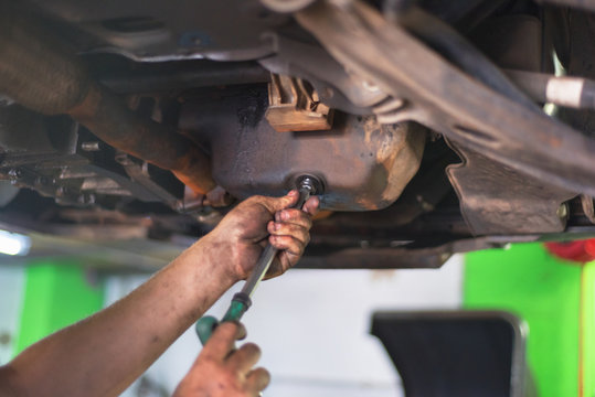 Car mechanic removing used engine oil