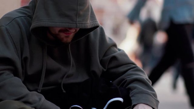 Close up homeless man sitting on street with sign eating people walk around honeliness sad social cardboard homeless beggar face poverty poor hungry dirty unemployed despair male slow motion portrait