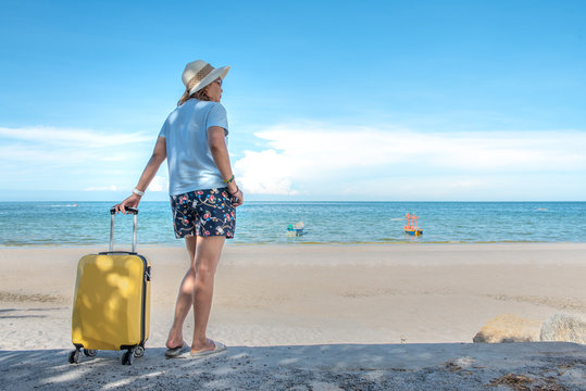 Young Asian woman with hat carrying suitcase at the beautiful sea beach in the weekend, travel concept.