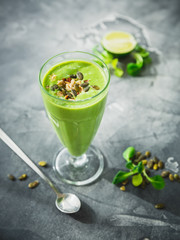 Tasty green smoothie made of spinach, banana and pumpkin seeds on dark.