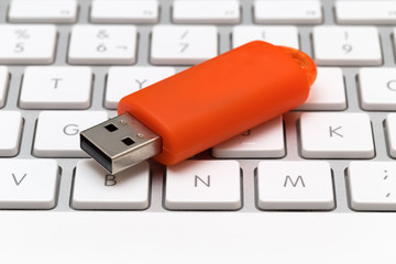 Orange USB pen drive arranged on white keyboard