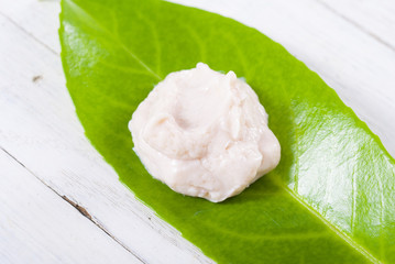 cosmetic cream on herbal leaf, white wood background