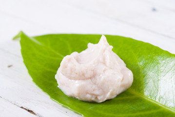 cosmetic cream on herbal leaf, white wood background