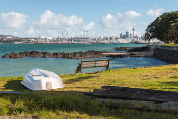 Auckland skyline from Davenport waterfront with white boat and bench in foreground