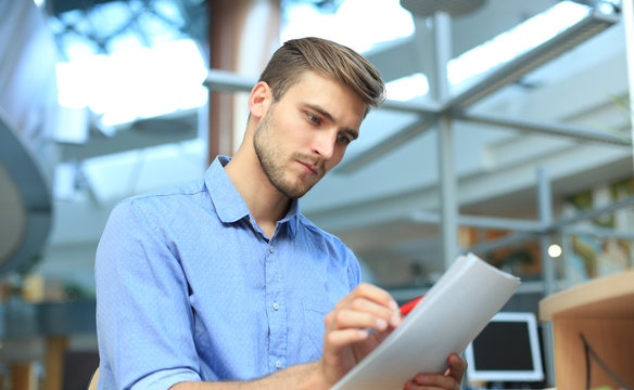 Young businessman reading paperwork at desk in office.