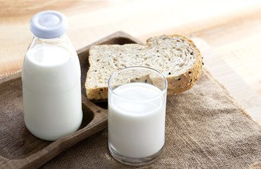 Bottle and glass of milk and bread placed on sackcloth on the wood table.
