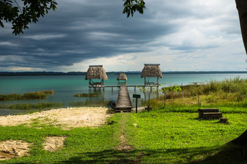 Hammocks on dock along the lake shore with dark blue cloudscape, El Remate, Peten, Guatemala