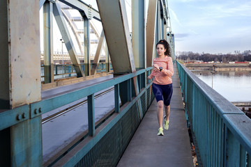 Young fit girl with long dark hair running on the bridge