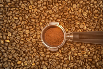 Metal espresso machine scoop with ground coffee on roasted coffee beans background