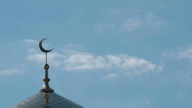 The bird flies by the side of the crescent on the minaret. A close-up of the clouds moving past the top of the Moslem mosque.