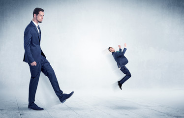 Fototapeta premium Big businessman kicking small businessman who is flying away with his briefcase on his hand 