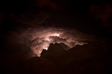 Lightning in the night sky is high in the mountains. Flashes of electrical discharges among the clouds and deafening thunder.