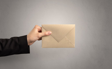 Female hand holding coloured and white envelope with empty wall background
