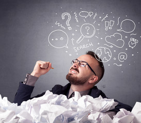Young businessman sitting behind crumpled paper with mixed doodles over his head