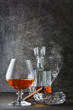 Strong alcoholic drink cognac in sniffer glass and decanter with smoking cigar in ashtray