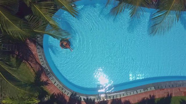 woman swims on buoy in pool under excotic trees