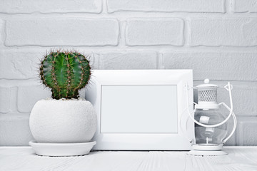Green cactus in flower pot, decorative lantern and mock-up of white frame with copy space for poster