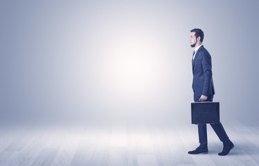 Fototapeta premium Successful businessman walking in front of an empty wall with briefcase on his hand 