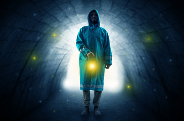 Fototapeta na wymiar Ugly man in raincoat walking with glowing lantern in a dark tunnel