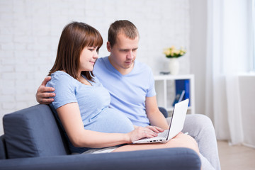 pregnant woman and her husband using laptop in living room