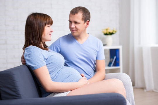 young beautiful pregnant couple sitting on sofa in living room