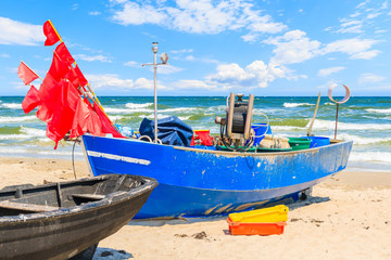 Naklejka na ściany i meble Traditional blue color fishing boat on sandy beach in Baabe town with big sea waves in background, Ruegen island, Baltic Sea, Germany