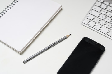 the keyboard, a clipboard, a pencil and a cell phone on a white surface