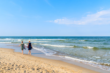 Couple of unidentified young women walking along beach in Baabe town from sand dune, Ruegen island, Baltic Sea, Germany - obrazy, fototapety, plakaty