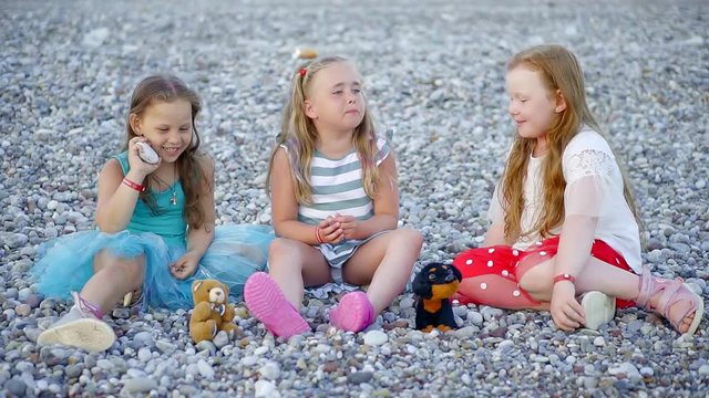 small funny girls play with soft toys on a rocky beach in the summer
