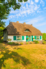 Fototapeta na wymiar Typical house with straw roof in warm sunset light and sunny blue sky near Ostseebad Sellin, Ruegen island, Baltic Sea, Germany
