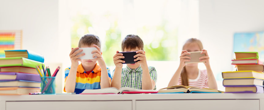 Children sitting in the room with smart phones. Pupils surfing at school