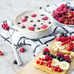 A table with a healthy summer breakfast - oatmeal with berries, currants and raspberries, and a sandwich with peanut butter, banana and various berries