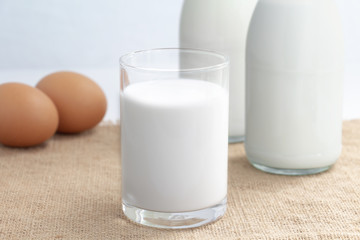 Two glass bottle and a cup of milk with egg on the sackcloth in the blue background  for food and healthy concept. with copy space for text.