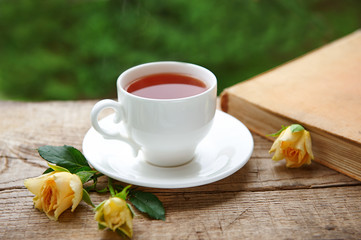 A cup of tea with yellow  flowers and close book outdoor