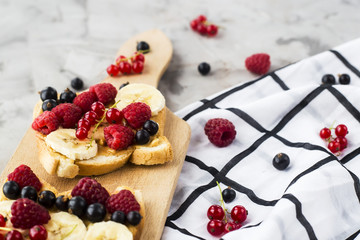 Sendvci with peanut butter, banana and raspberries and currants on a wooden board on a gray table. Vegan healthy breakfast