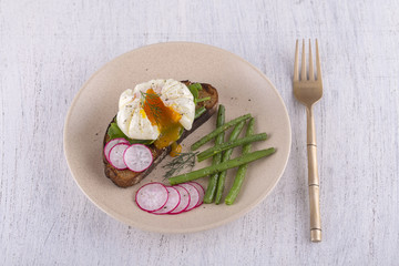 Poached egg on a piece of bread with fried green beans, radish and arugula on a plate