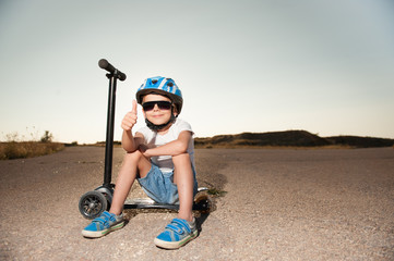 cute kid with thumb up finger wearing sunglasses and helmet sitting on scooter © ruslanshug