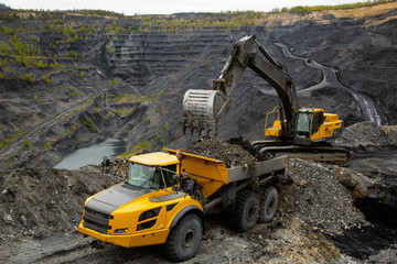 Excavator loads coal in a articulated dump truck. Heavy mining industry.