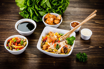 Roasted meat, rice noodles and vegetables on wooden background