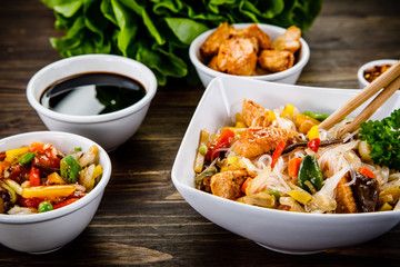 Roasted meat, rice noodles and vegetables on wooden background