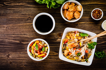 Roasted meat, rice noodles and vegetables on wooden background