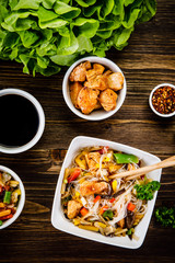 Roasted meat, rice noodles and vegetables on wooden background