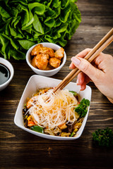 Roasted meat, rice noodles and vegetables on wooden background