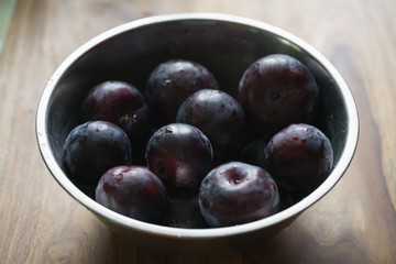 freshly washed big plums in a steel bowl on wood table